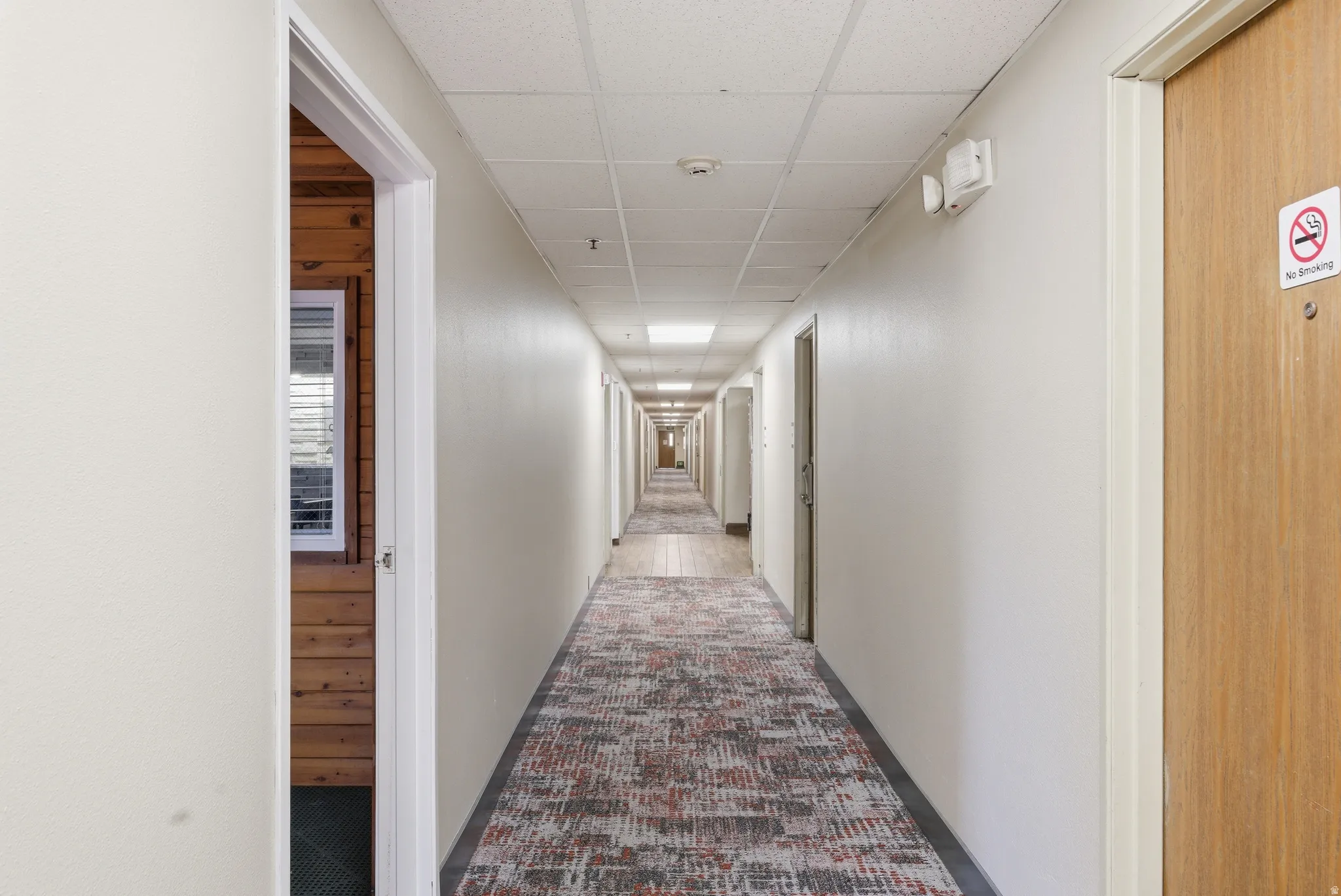 Corridor featuring a paneled ceiling and dark carpet