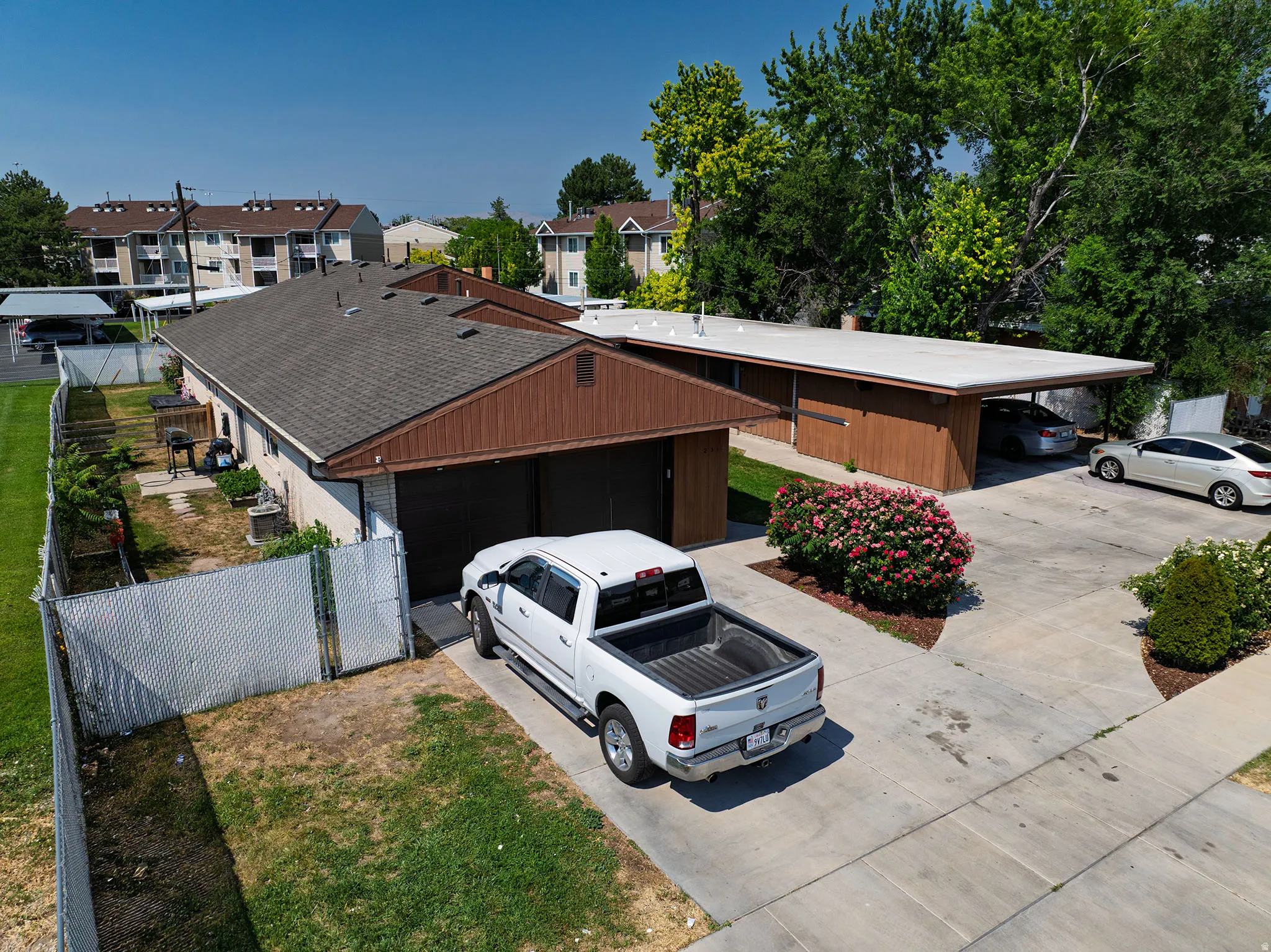 Asphalt shingle roofing, attached carport, concrete driveway, garage door, and mature landscaping with flowering shrubs