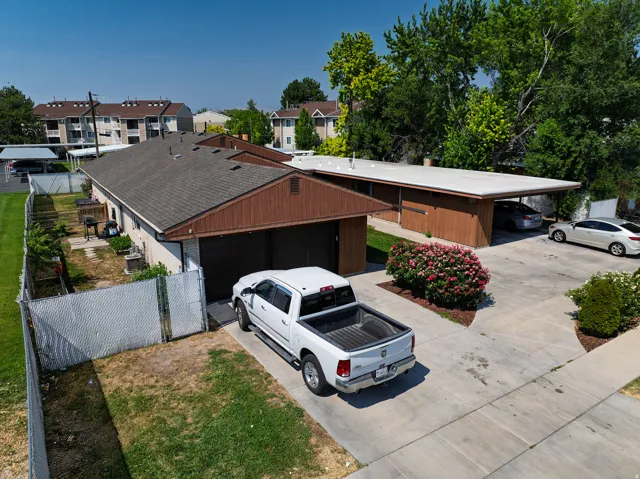 Asphalt shingle roofing, attached carport, concrete driveway, garage door, and mature landscaping with flowering shrubs
