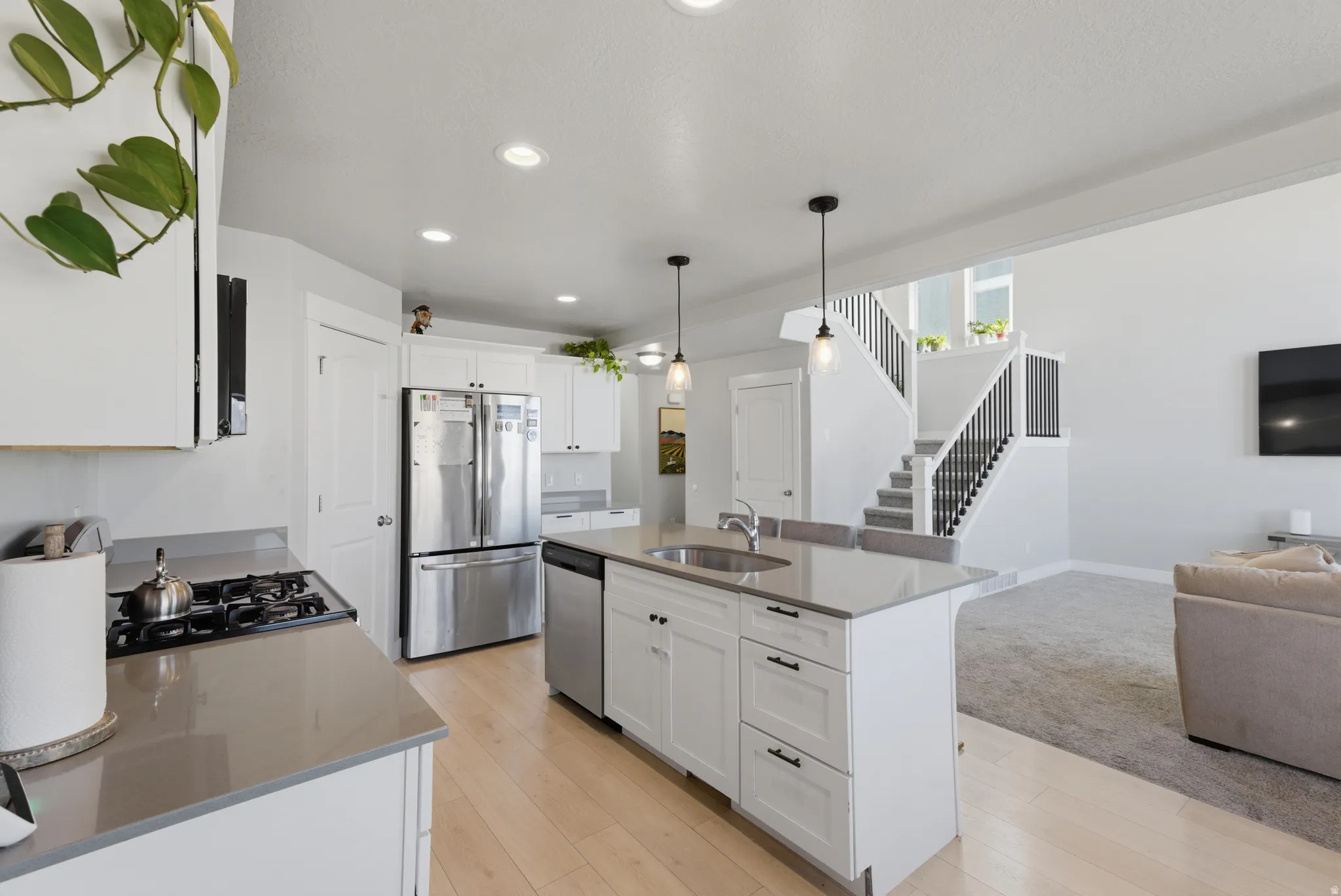 Kitchen featuring open floor plan, stainless steel appliances, an island with sink, white cabinetry, and decorative light fixtures