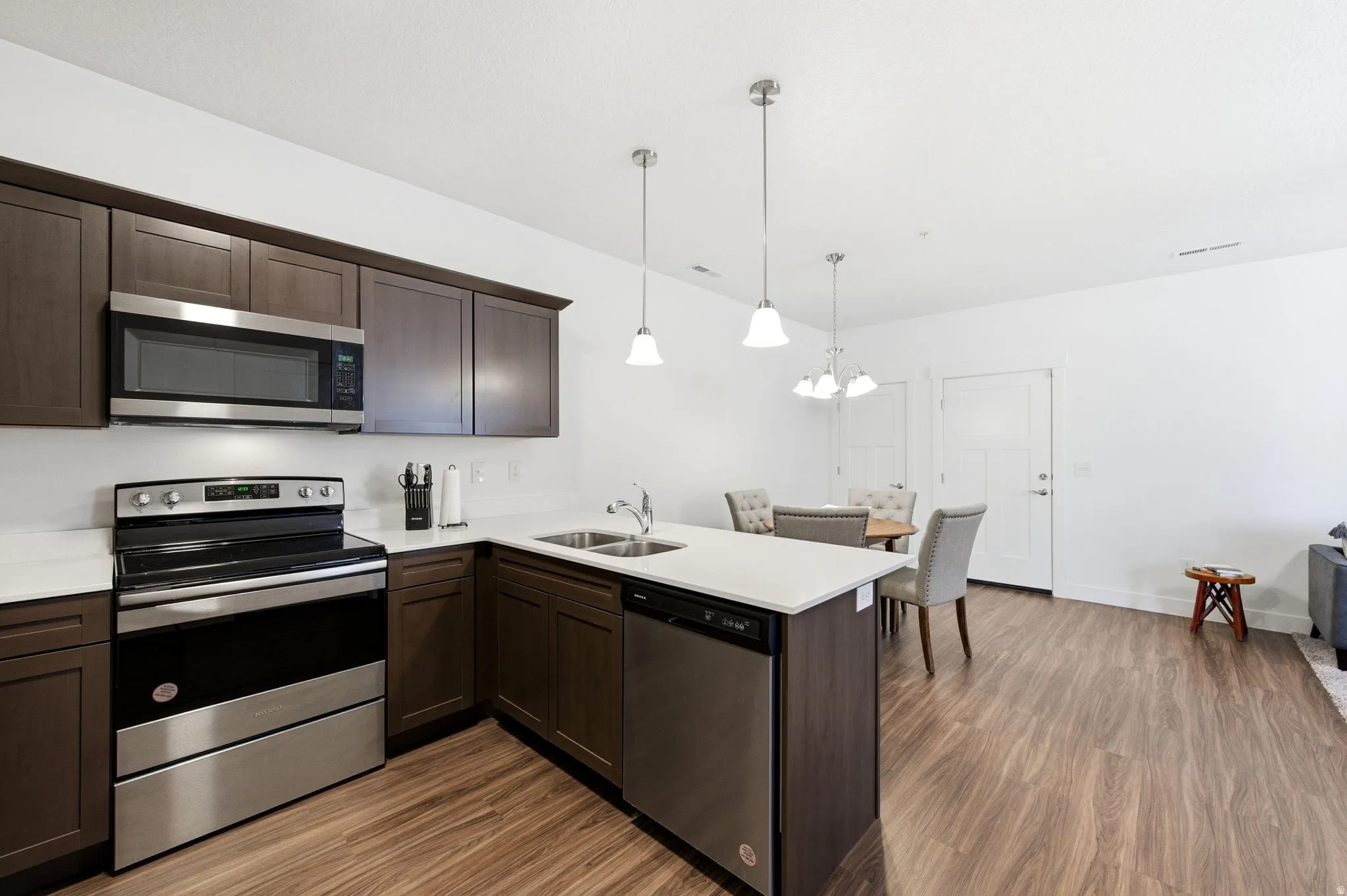 Kitchen featuring stainless steel appliances, a peninsula, dark wood finish cabinetry, hanging lights, and dark wood-style floors