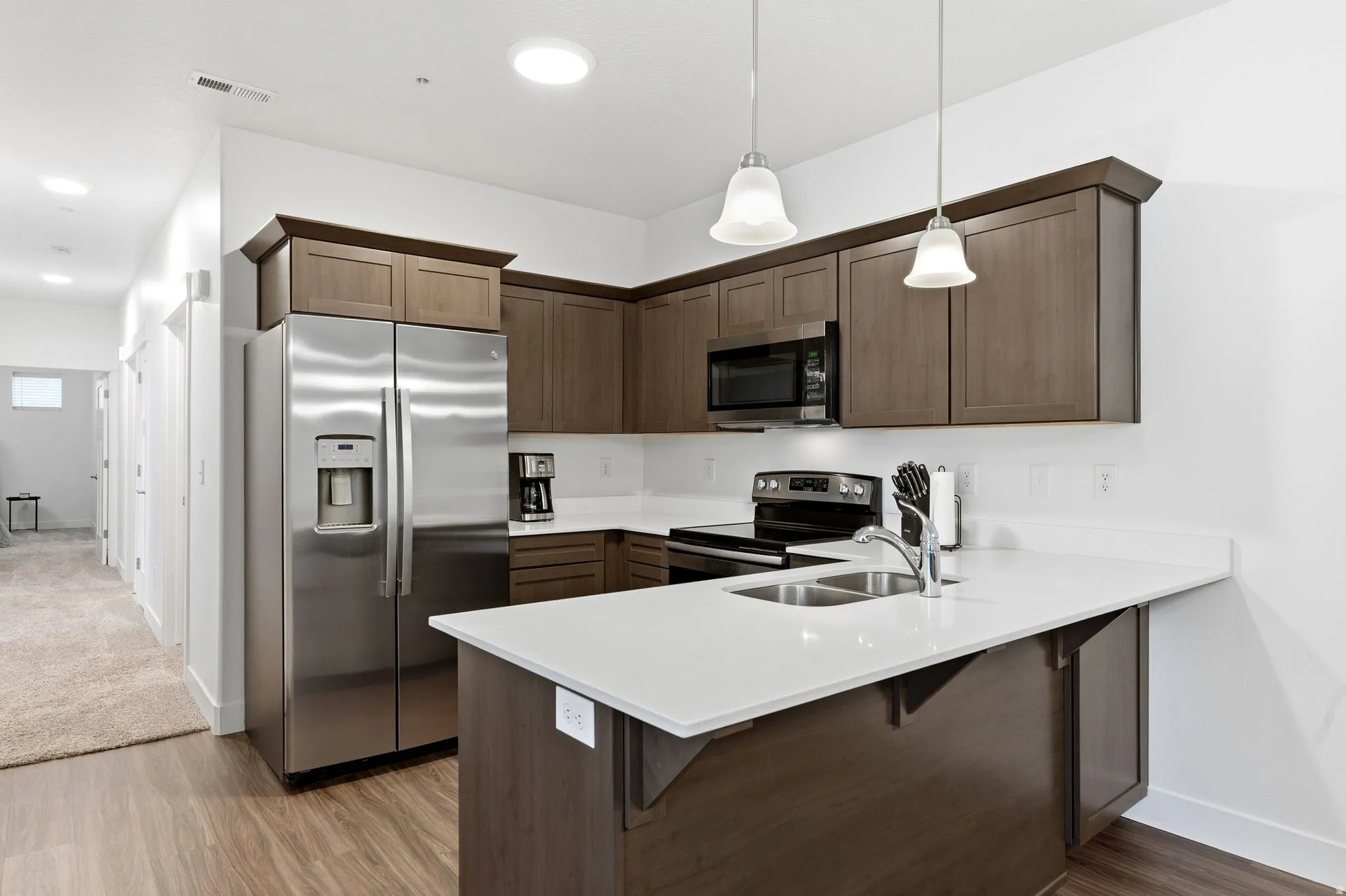Kitchen with a kitchen bar, stainless steel appliances, a peninsula, dark wood finish cabinetry, and light wood-style floors