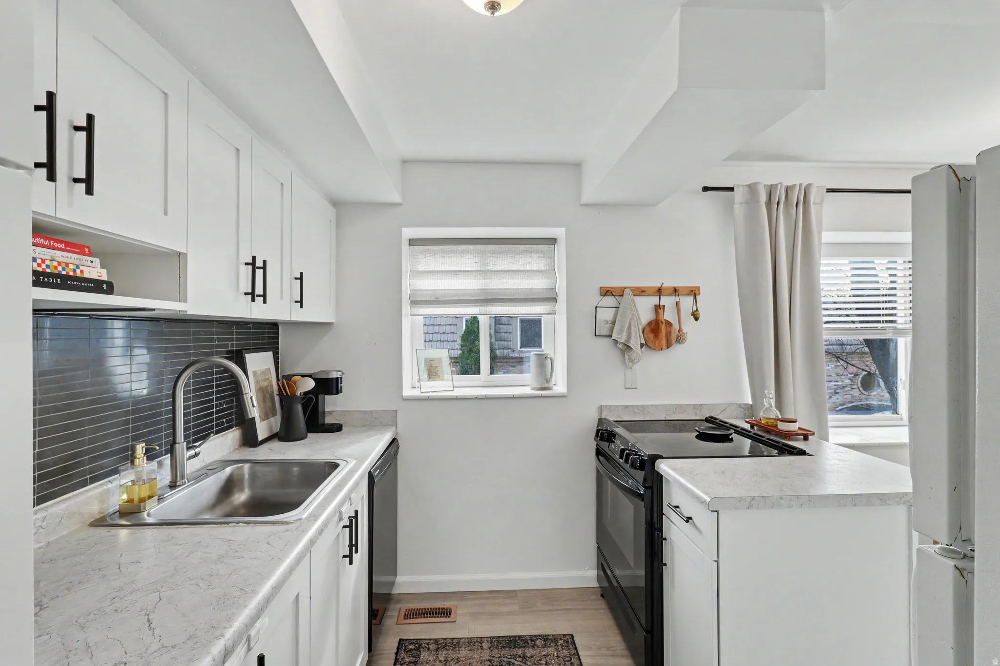 Kitchen with black electric range oven, white cabinets, a peninsula, tasteful backsplash, and light countertops