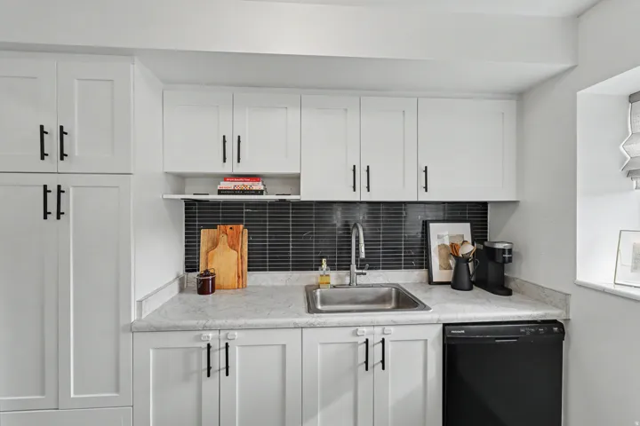 Kitchen with white cabinetry, dishwasher, light countertops, and backsplash