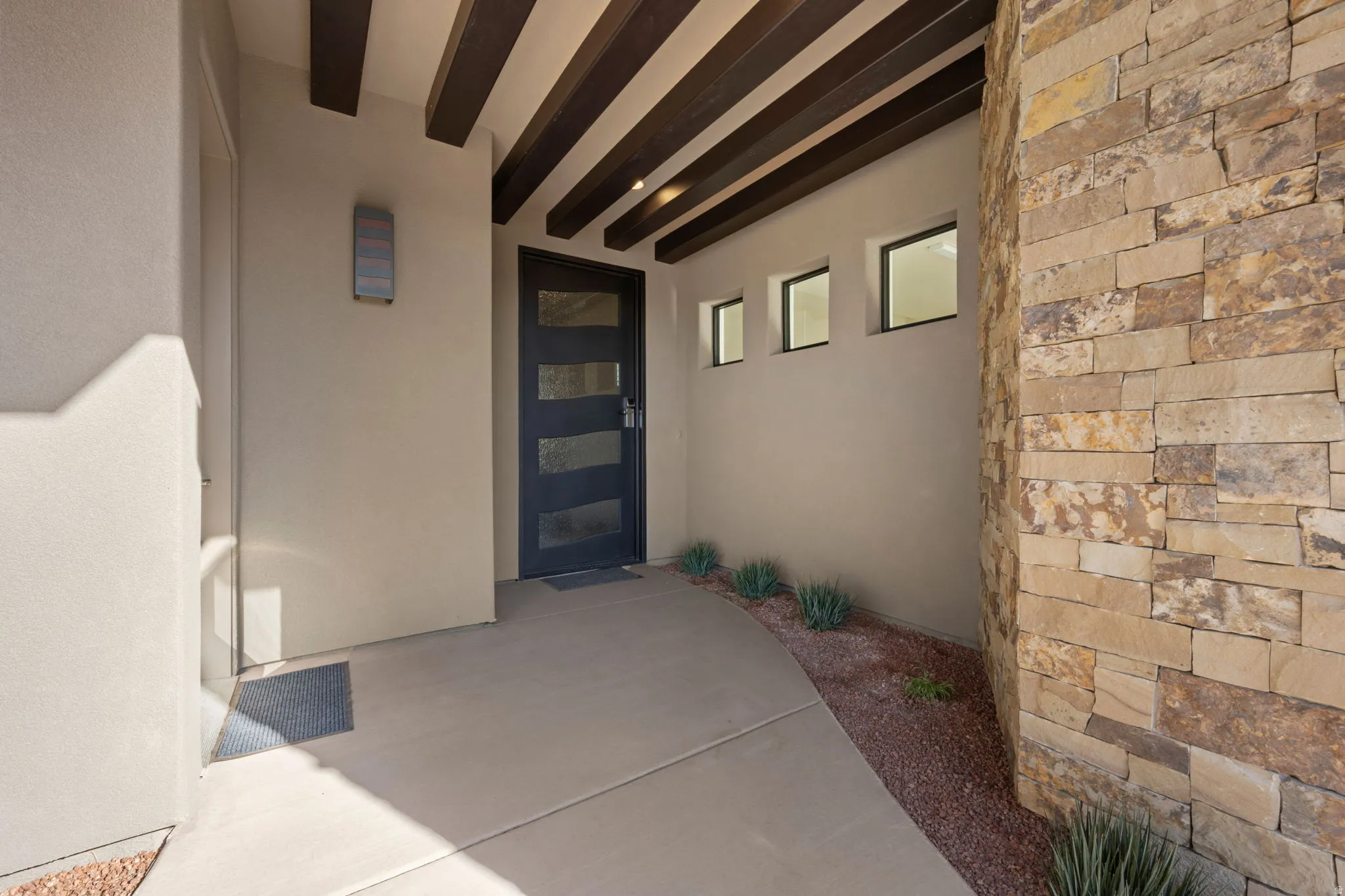 Property entrance with stucco siding, stone siding, and a patio area