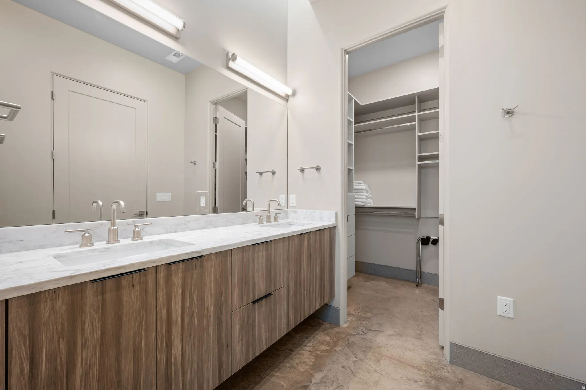 Bathroom featuring double vanity, concrete floors, and a walk in closet