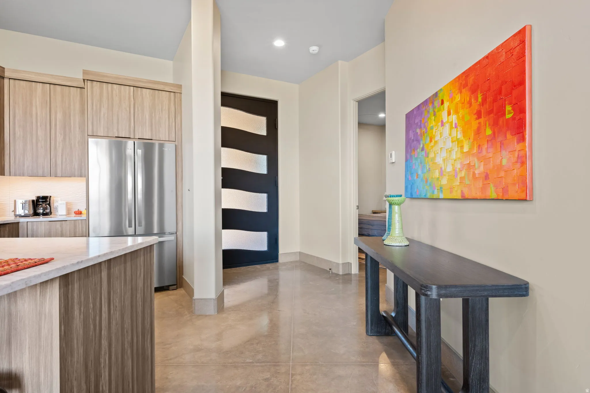 Kitchen featuring modern cabinets, freestanding refrigerator, light wood finish cabinetry, finished concrete flooring, and light stone countertops