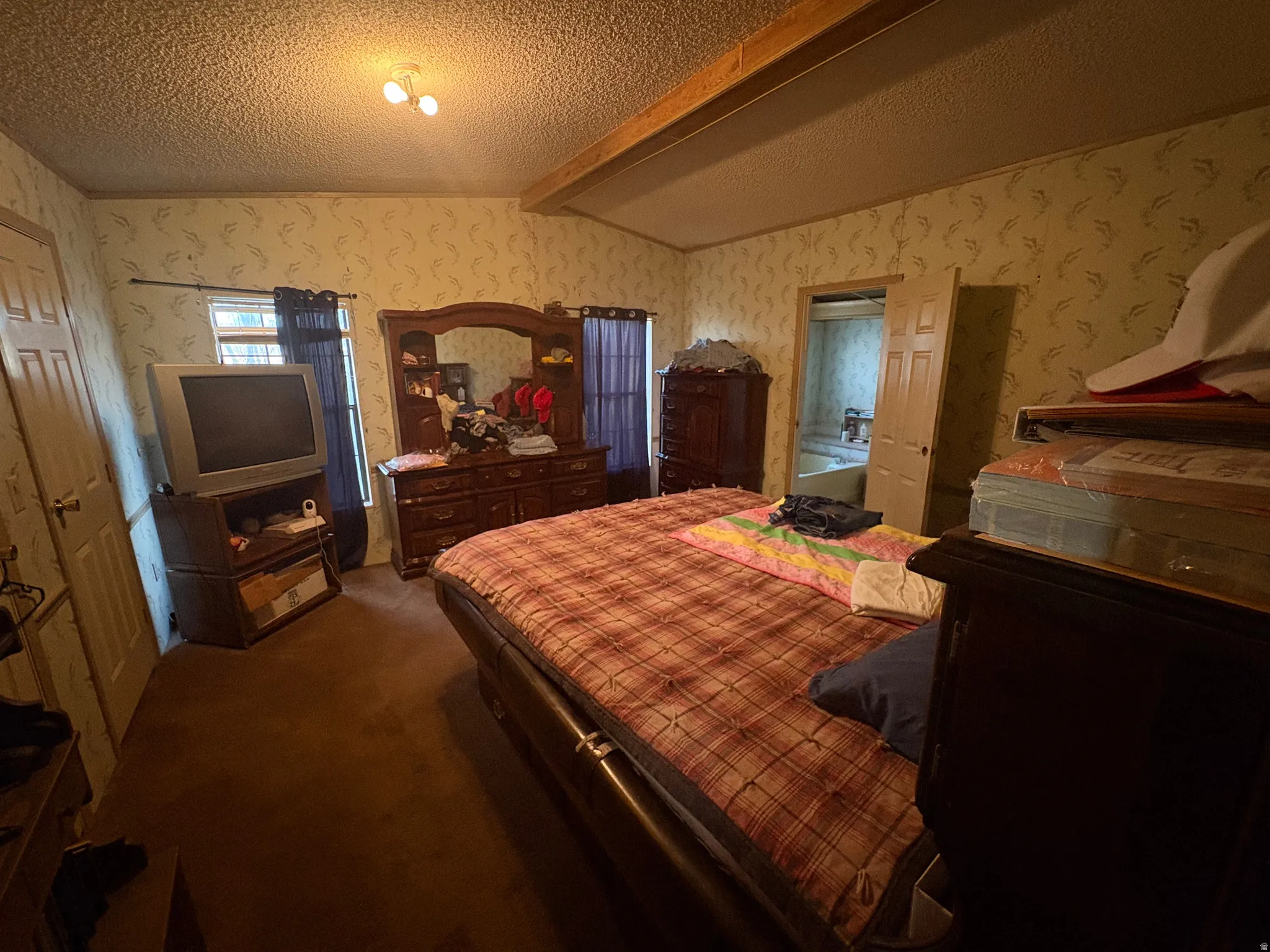 Bedroom with beamed ceiling, dark colored carpet, and wallpapered walls