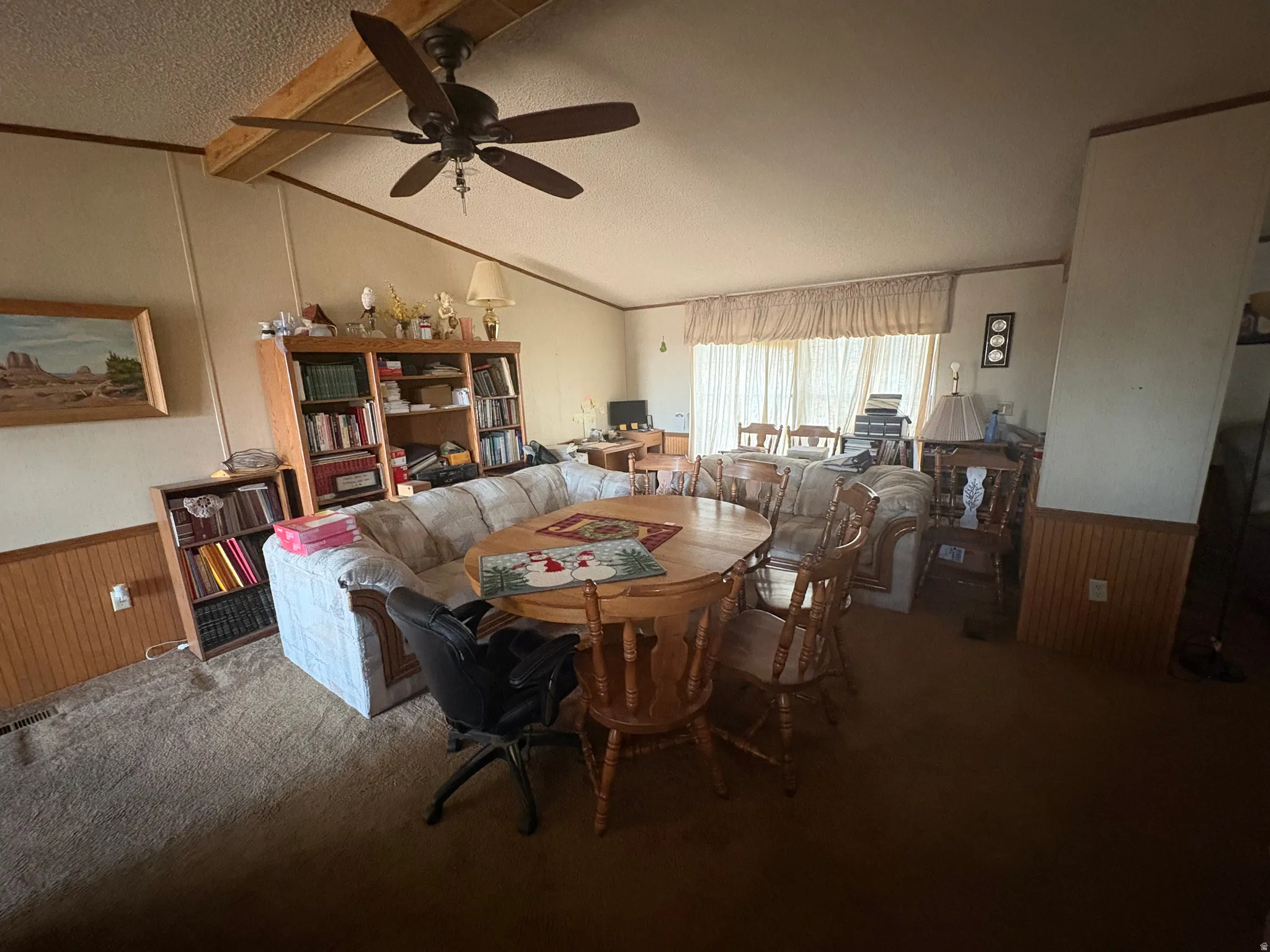 Dining area with a wainscoted wall, wooden walls, carpet floors, beam ceiling, and ceiling fan