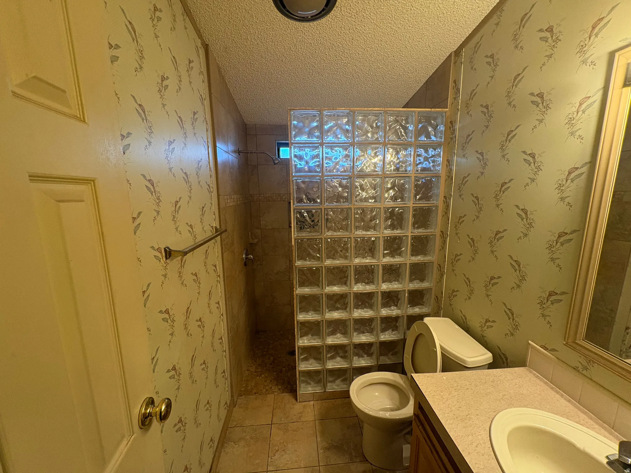 Full bath with wallpapered walls, a textured ceiling, vanity, a walk in shower, and tile patterned floors
