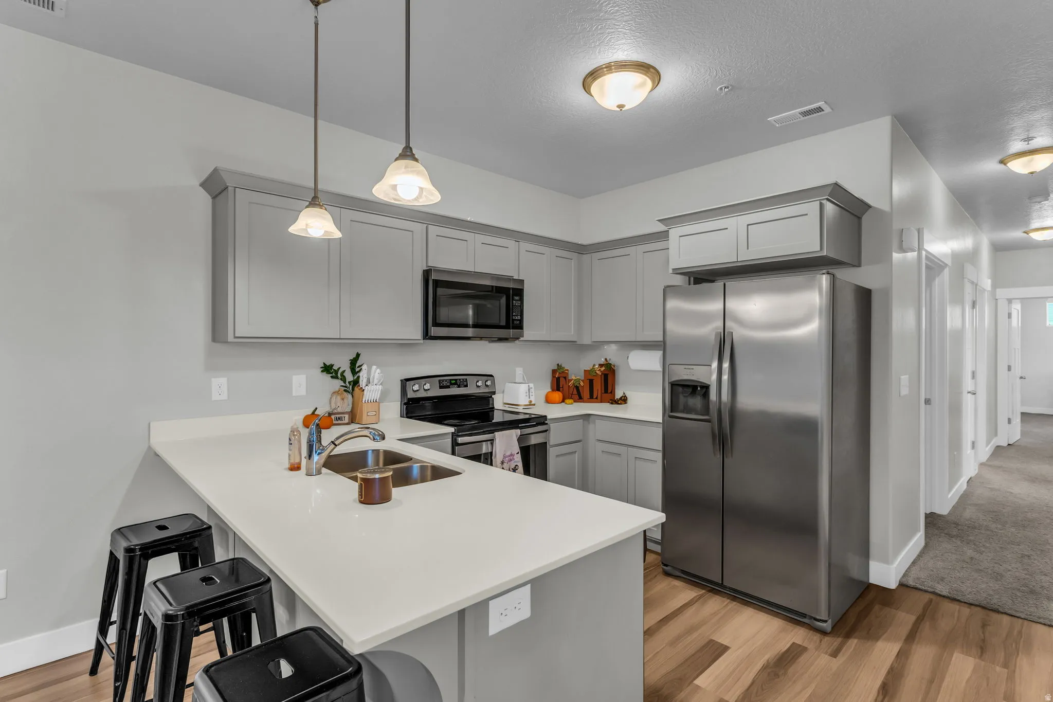 Kitchen with a kitchen breakfast bar, stainless steel appliances, gray cabinetry, a peninsula, and light wood finished floors