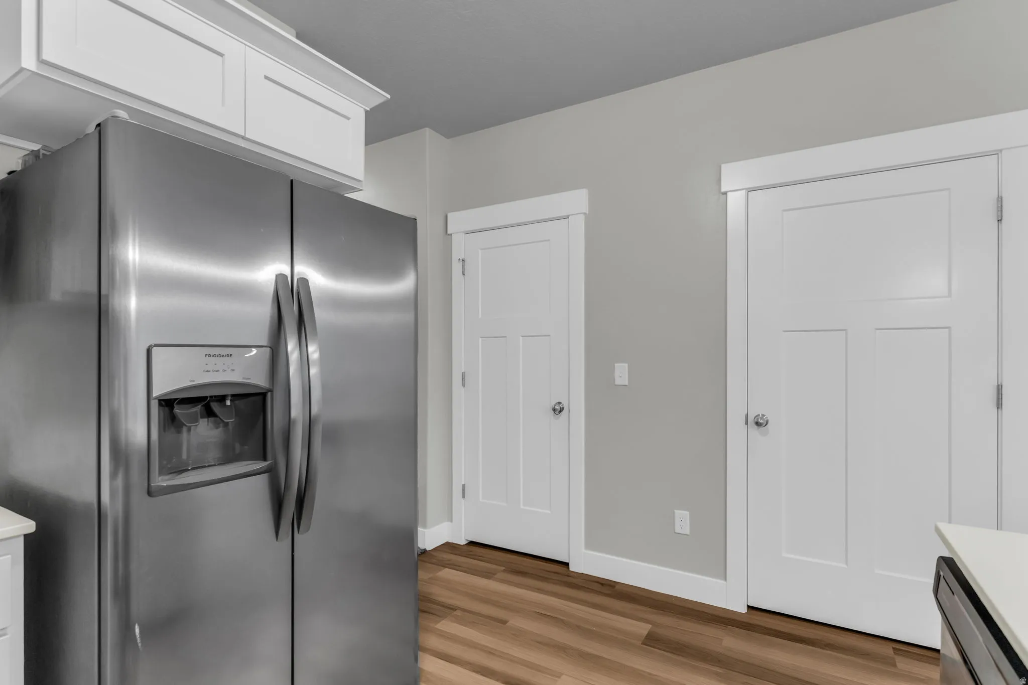 Kitchen featuring stainless steel fridge with ice dispenser, light wood-type flooring, white cabinets, and light countertops