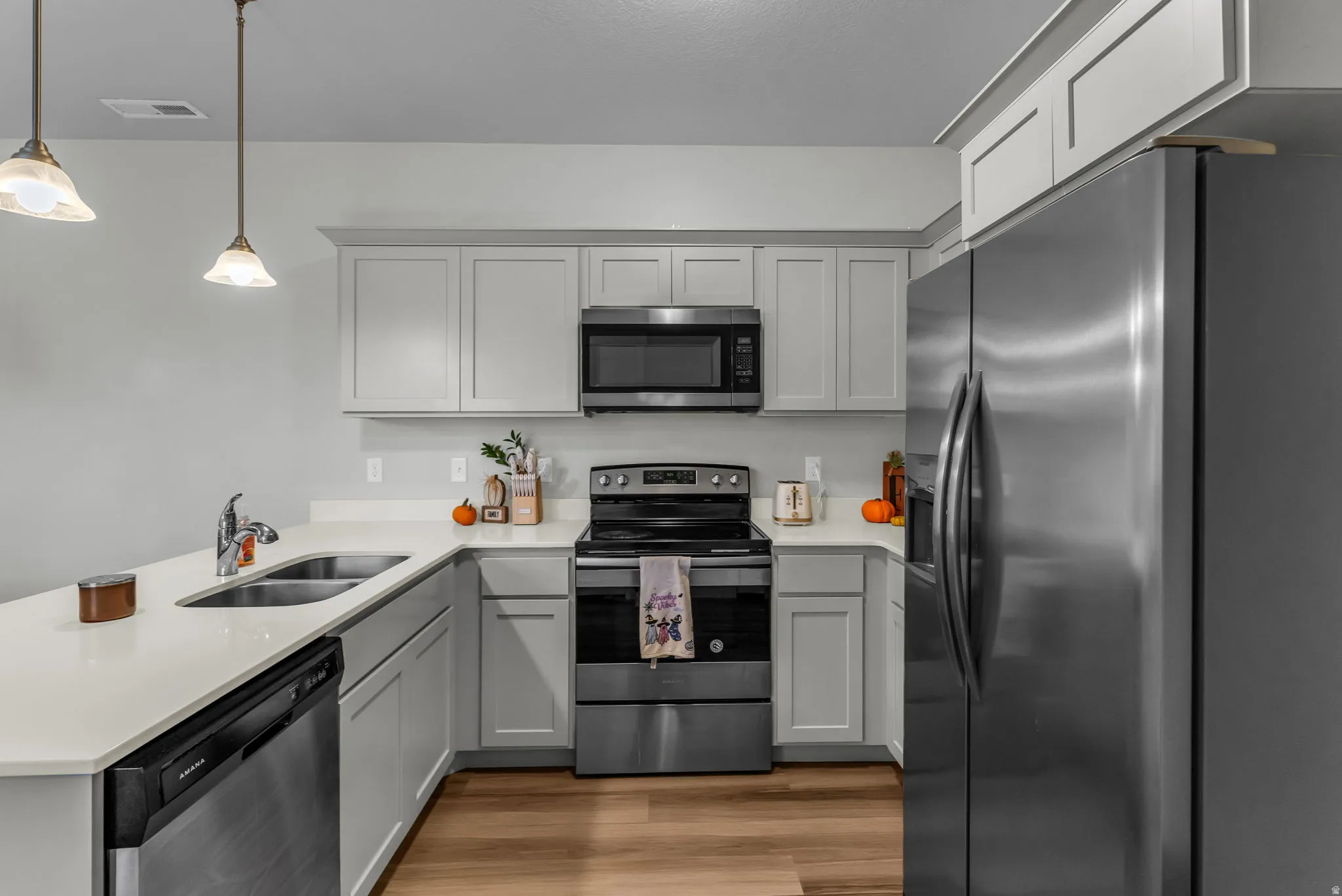 Kitchen featuring stainless steel appliances, a peninsula, gray cabinets, light stone counters, and pendant lighting