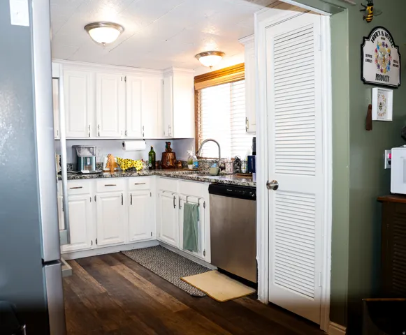 Kitchen with white cabinetry, stainless steel appliances, dark wood-style floors, and dark stone counters