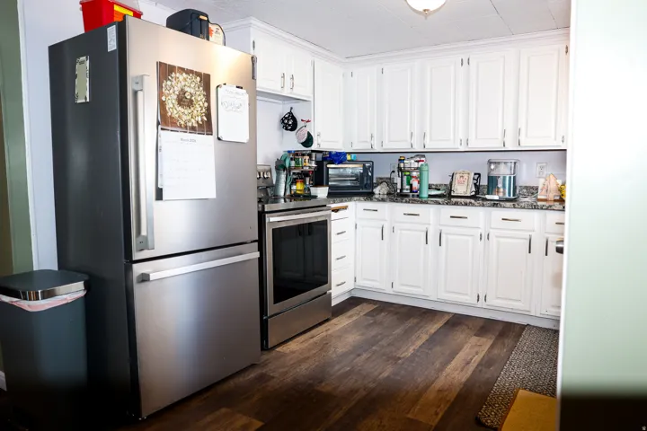 Kitchen with stainless steel appliances, white cabinetry, dark wood-style floors, and dark stone counters