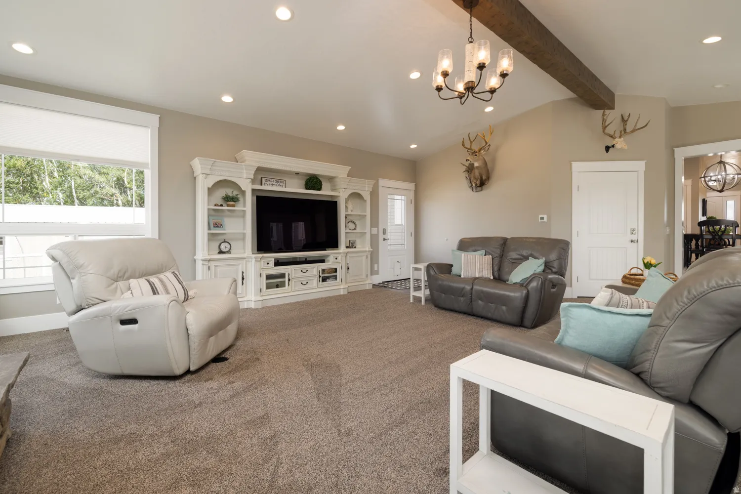 Carpeted living room featuring a chandelier, plenty of natural light, and vaulted ceiling with beams