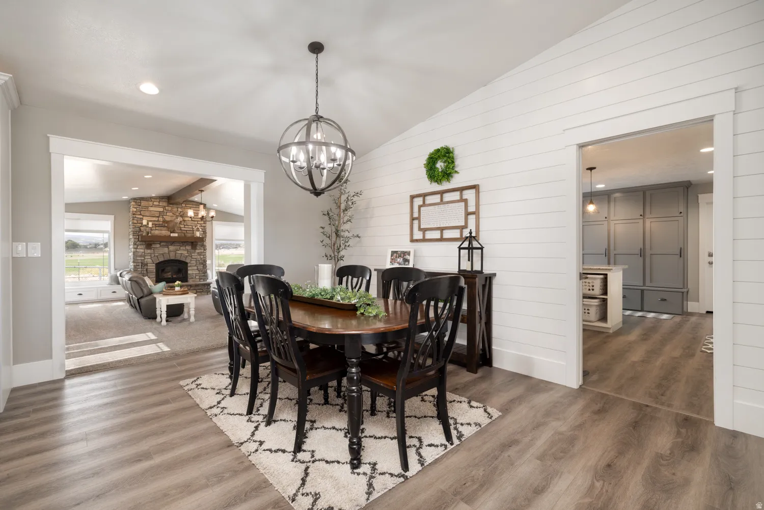 Dining area with vaulted ceiling, a stone fireplace, wood finished floors, wood walls, and hanging lights