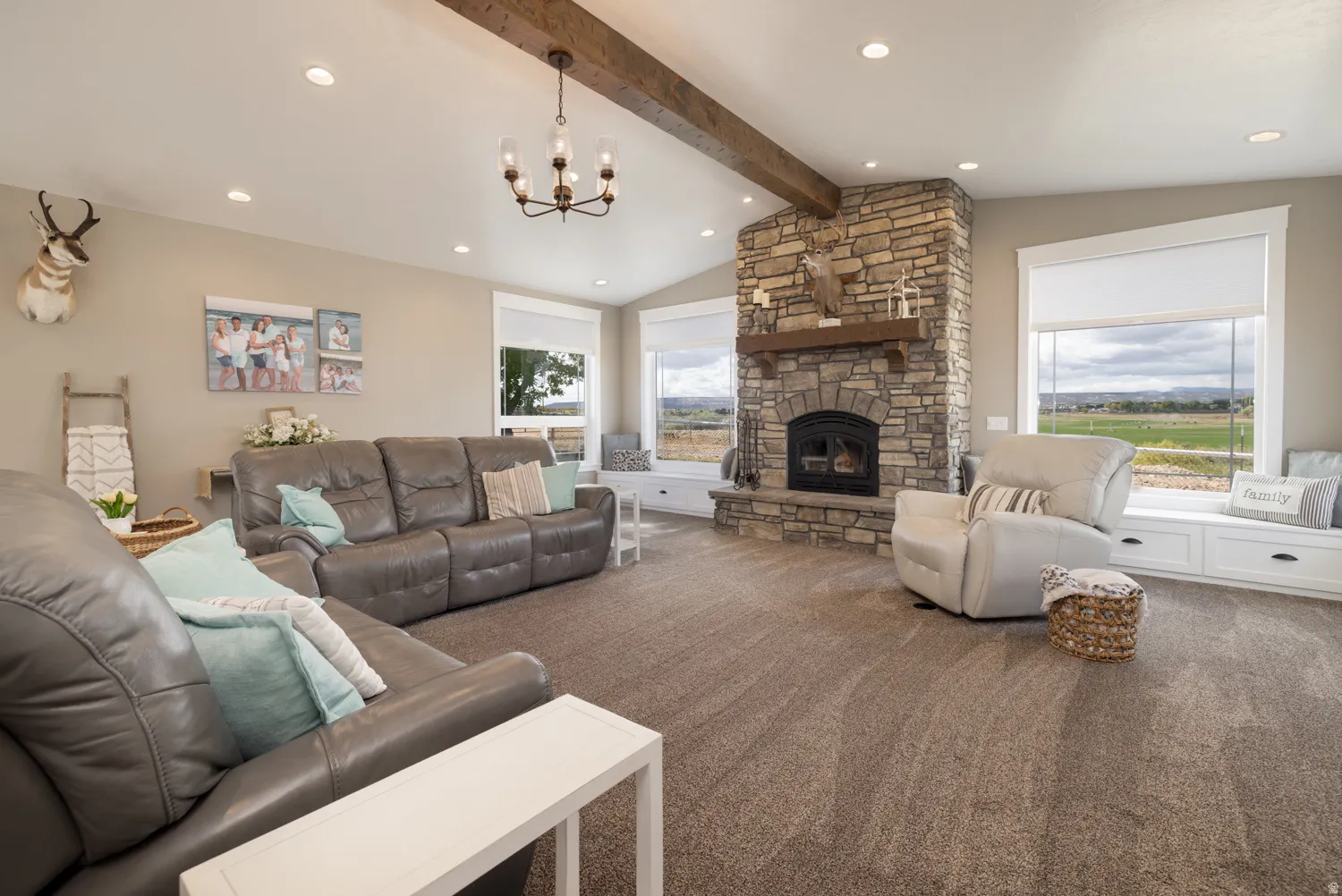 Living room featuring vaulted ceiling with beams, a stone fireplace, carpet flooring, and a chandelier