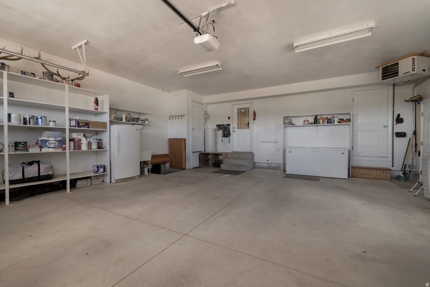 Garage featuring a heating unit, freestanding refrigerator, and a garage door opener