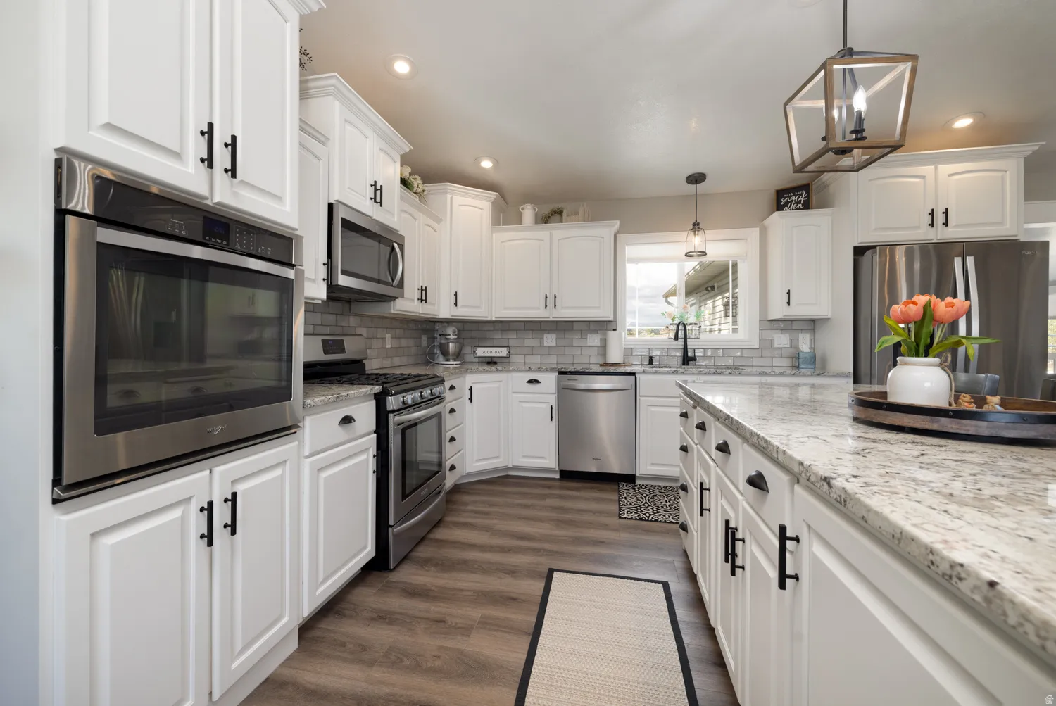 Kitchen with stainless steel appliances, light stone countertops, dark wood-style flooring, and white cabinets