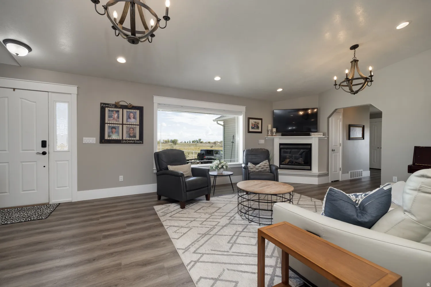 Living area featuring a chandelier, wood finished floors, a glass covered fireplace, and arched walkways