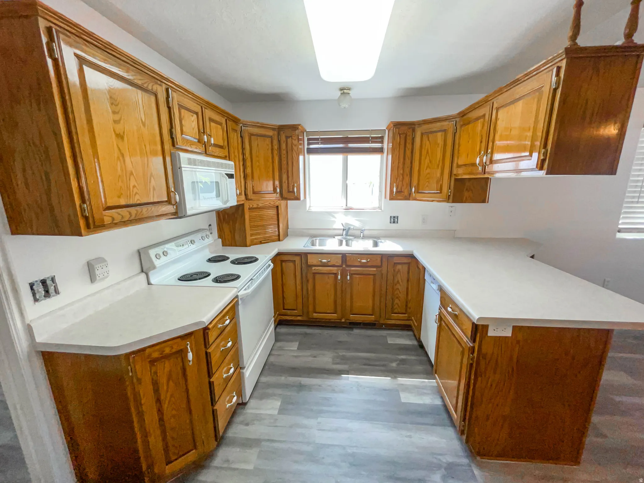 Kitchen featuring white appliances, wood finish cabinets, light countertops, and a peninsula