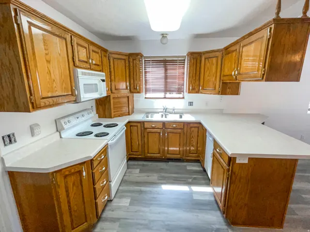 Kitchen with wood finish cabinetry, white appliances, light countertops, a peninsula, and dark wood-style floors