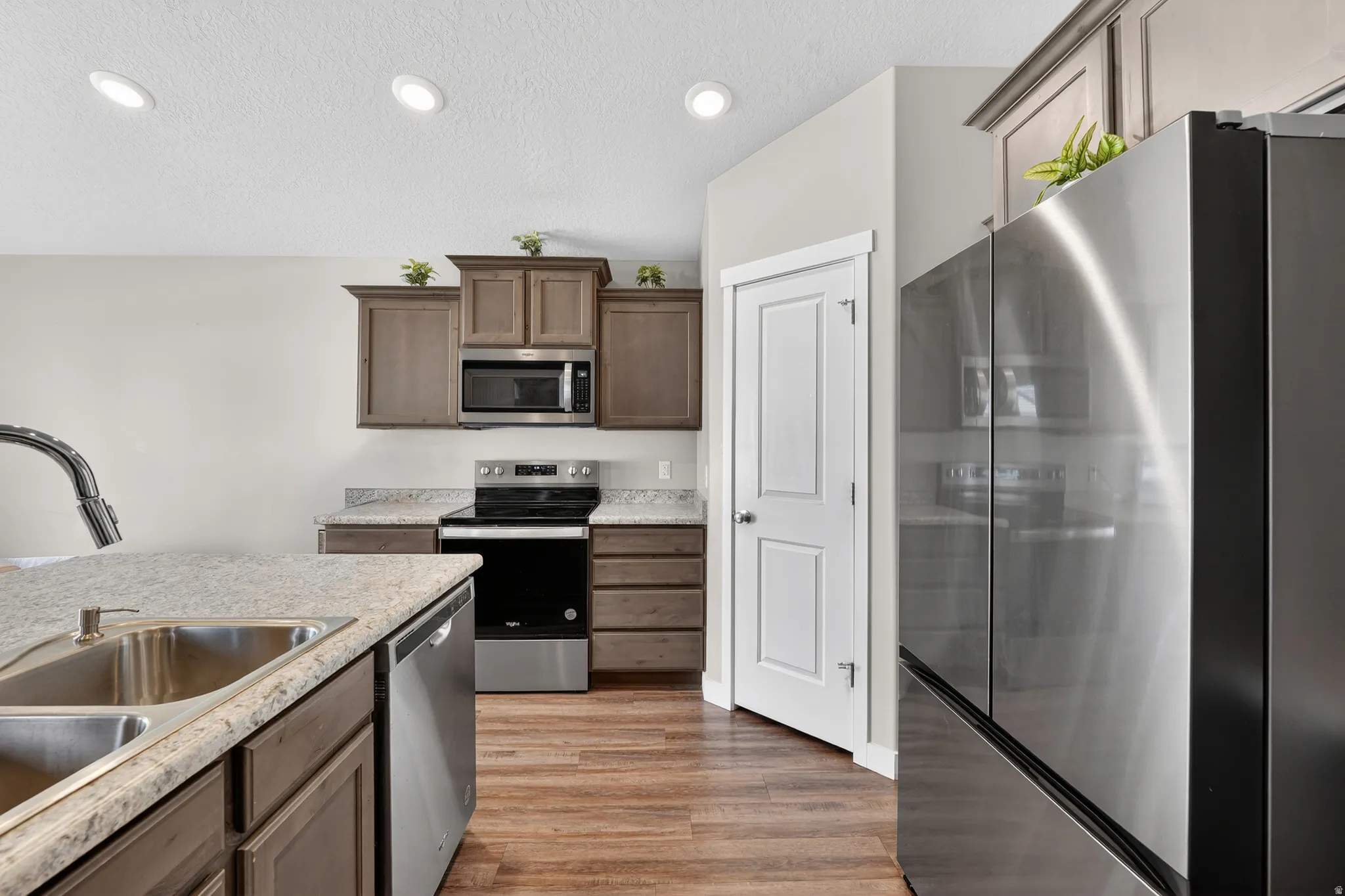 Kitchen with stainless steel appliances, light wood-type flooring, a textured ceiling, light stone countertops, and recessed lighting