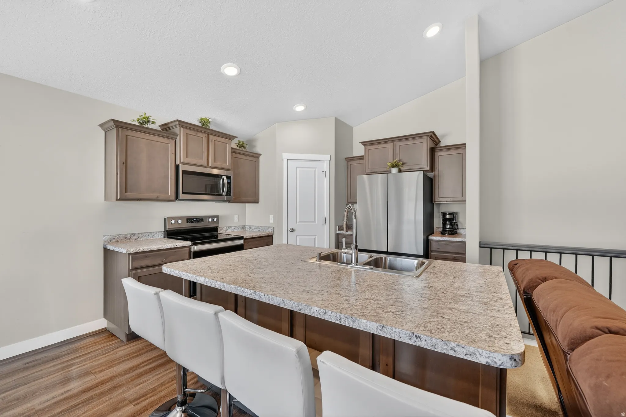 Kitchen featuring stainless steel appliances, a kitchen bar, light countertops, an island with sink, and light wood-type flooring
