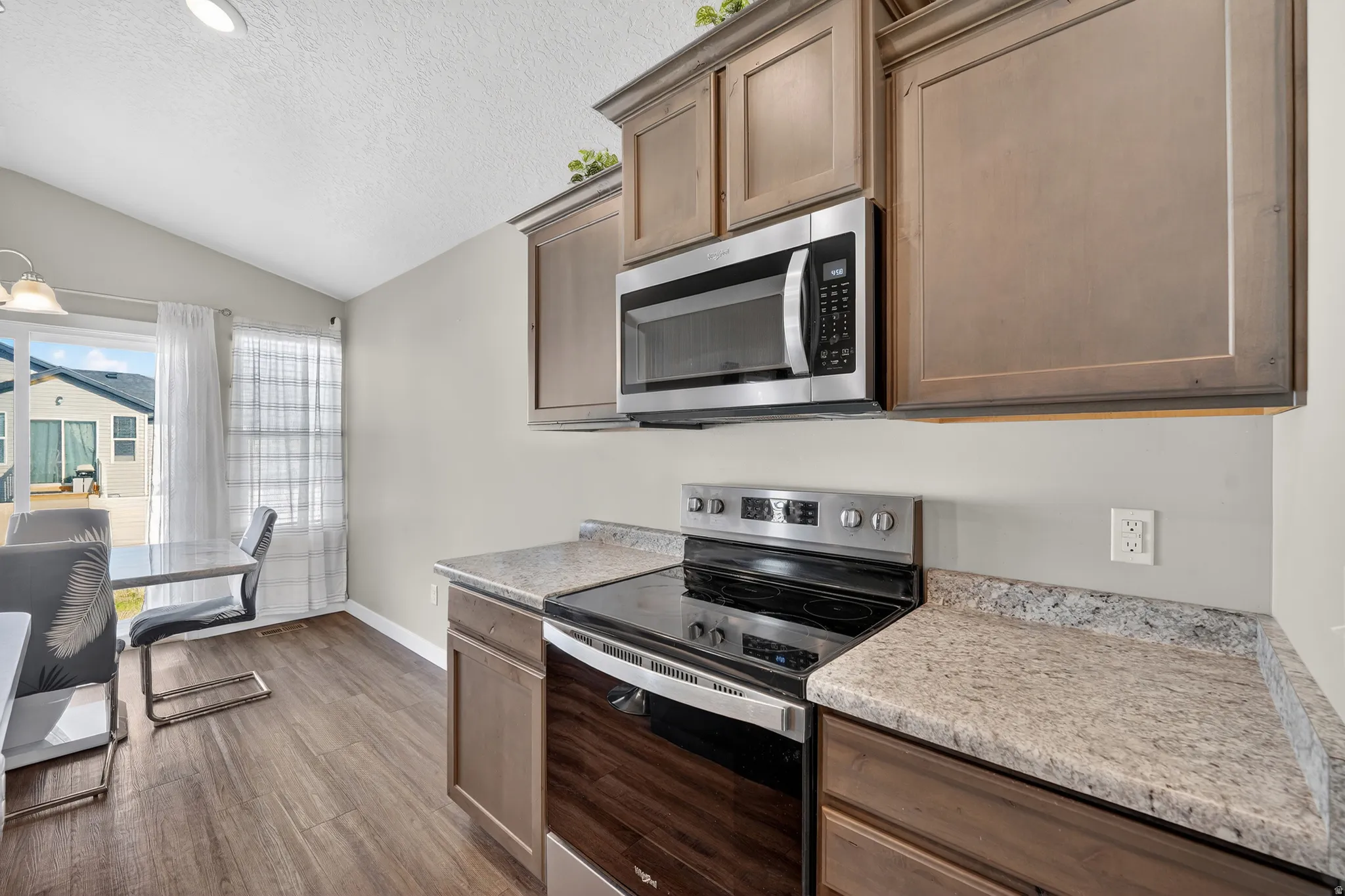 Kitchen with stainless steel appliances, dark wood-type flooring, and light stone countertops