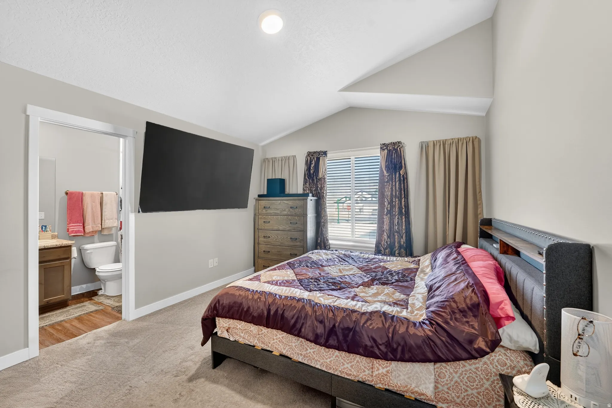 Bedroom with light colored carpet, vaulted ceiling, and connected bathroom