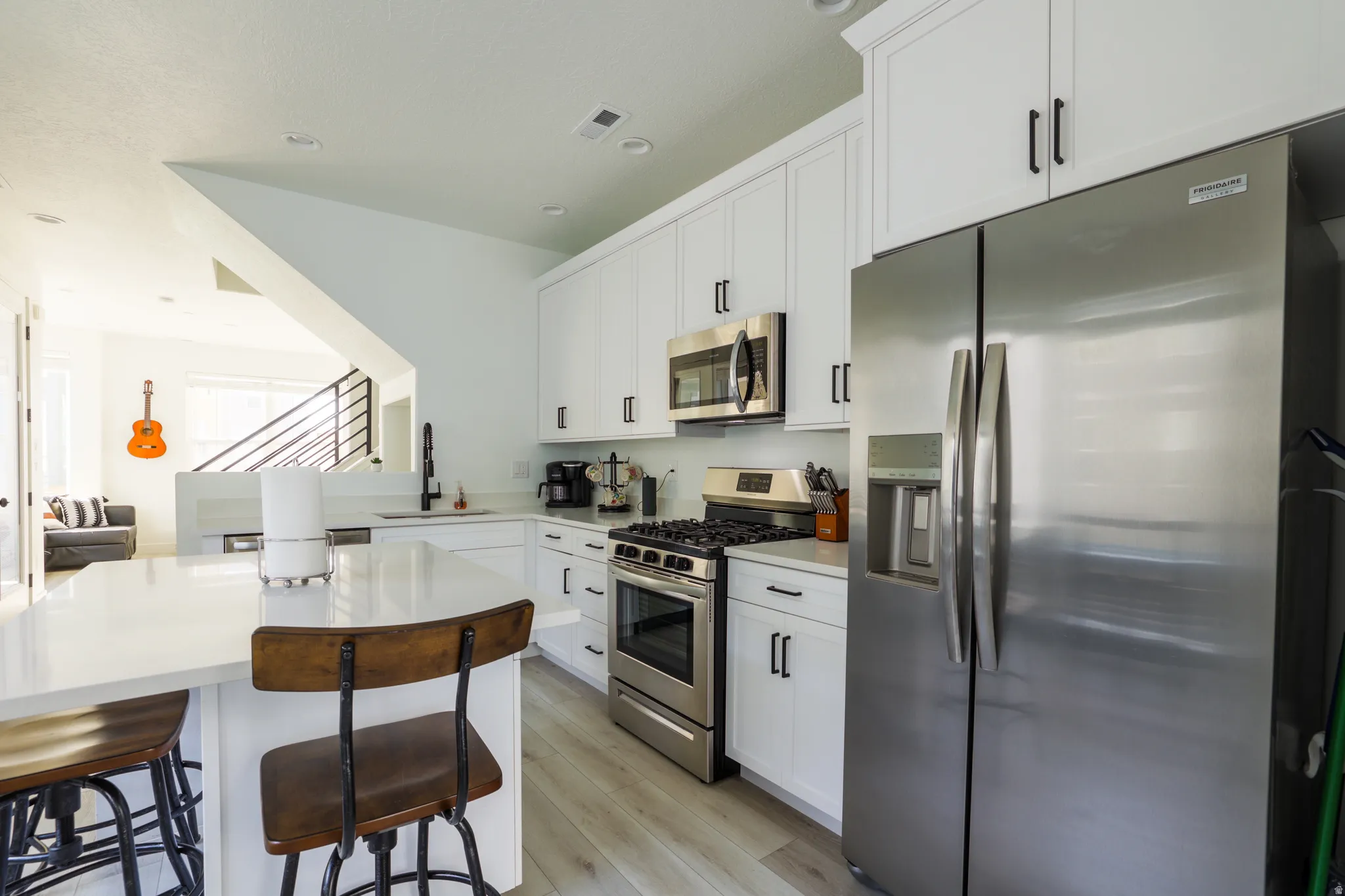 Kitchen featuring stainless steel appliances, white cabinets, light wood-style flooring, a breakfast bar area, and recessed lighting