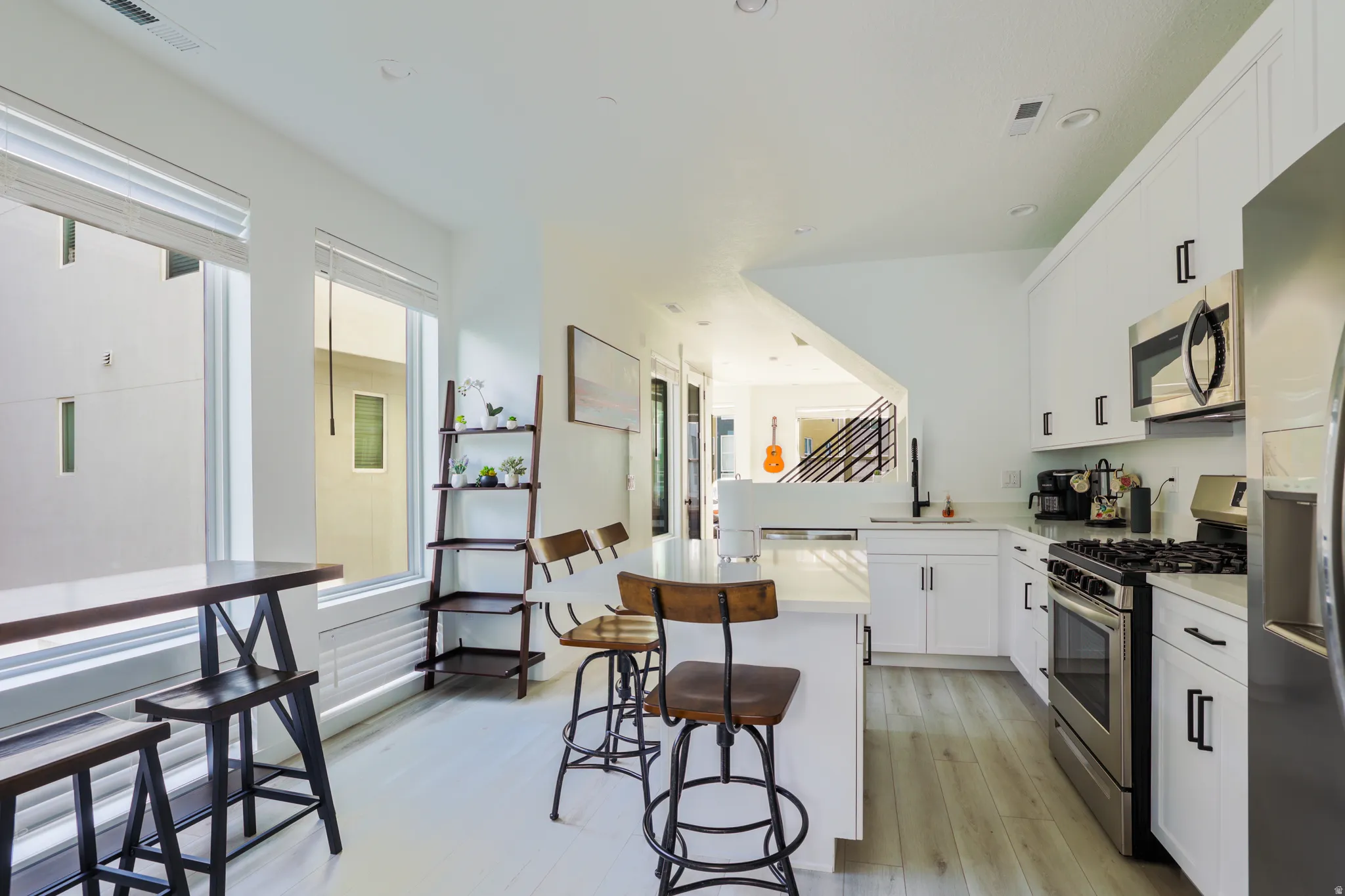 Kitchen featuring stainless steel appliances, white cabinetry, a kitchen bar, light wood-type flooring, and a center island