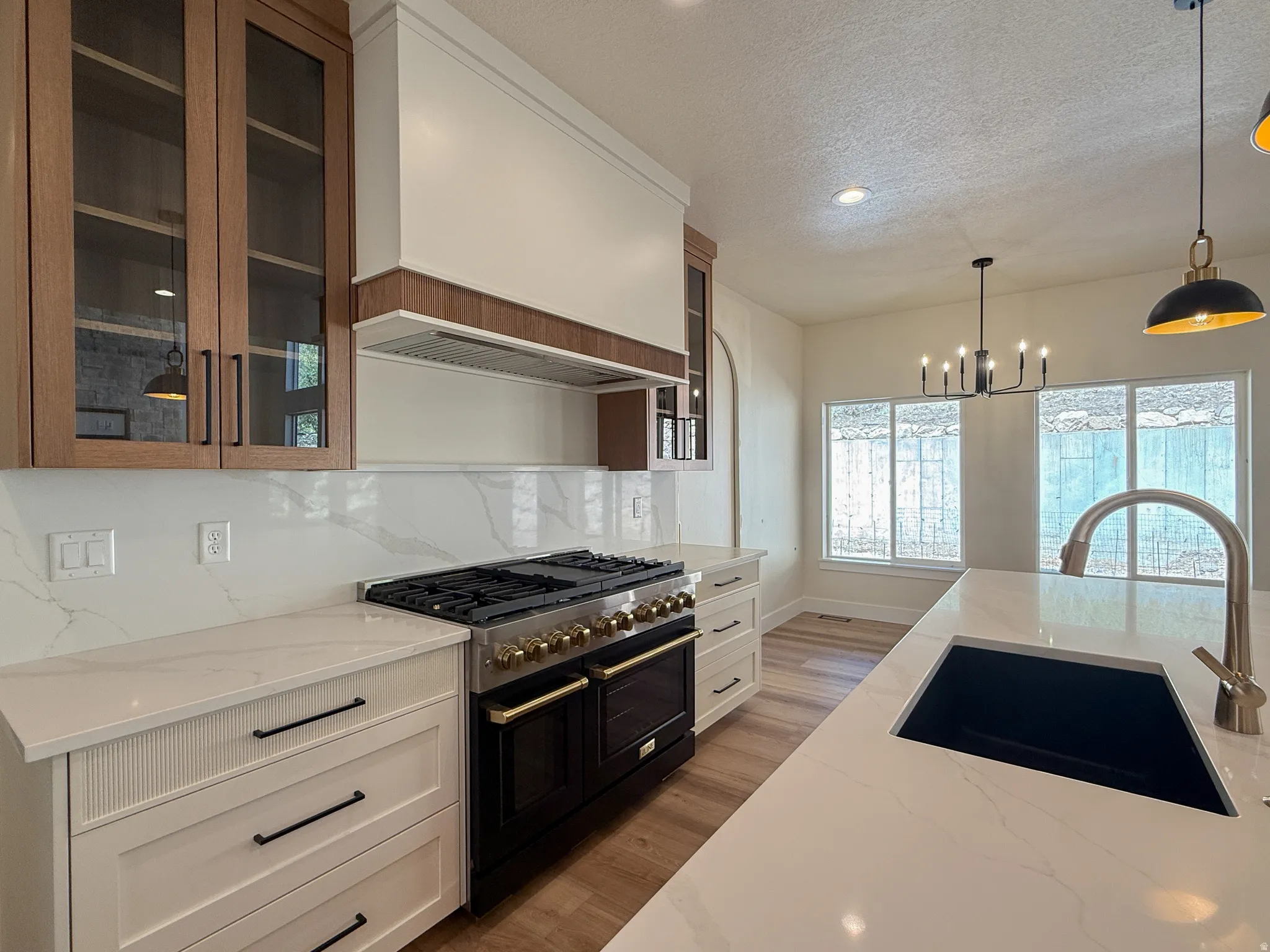 Kitchen with double oven range, glass fronted cabinets, light stone counters, light wood finished floors, and suspended lighting