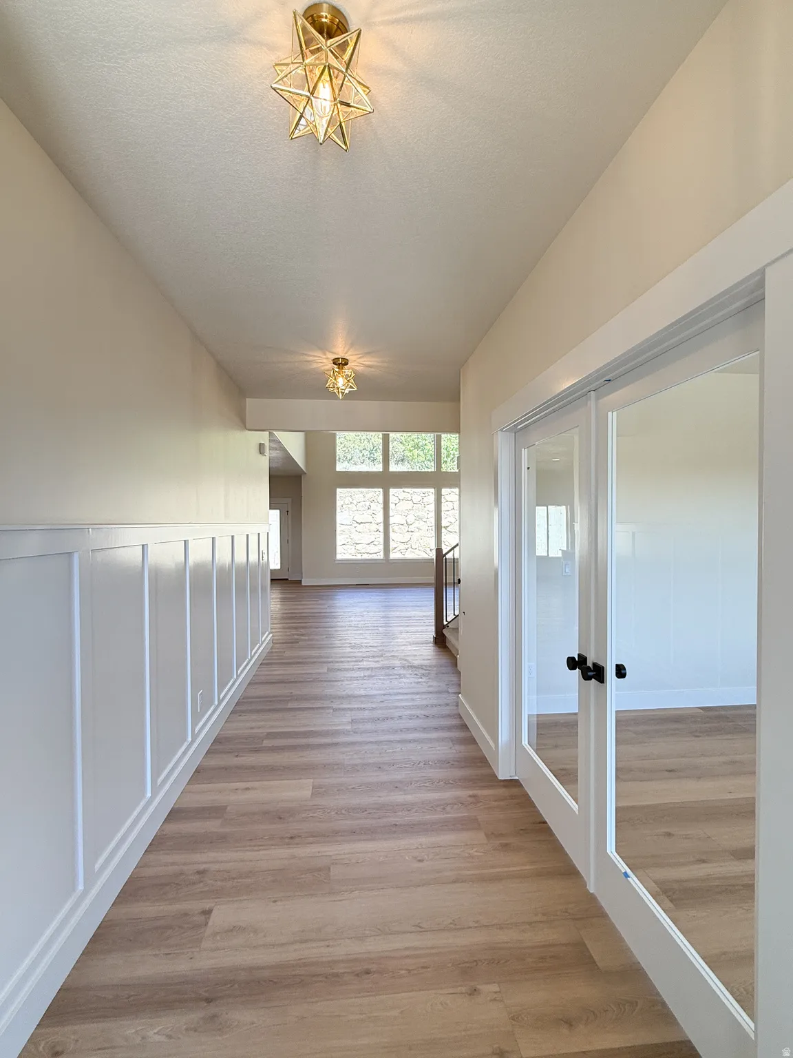 Corridor featuring french doors, light wood-type flooring, a textured ceiling, and a decorative wall