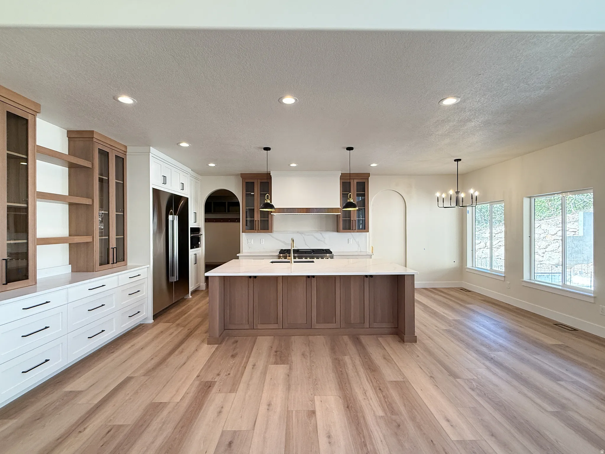 Kitchen with glass fronted cabinets, a spacious island, stainless steel built in fridge, dual tone cabinetry, and a textured ceiling