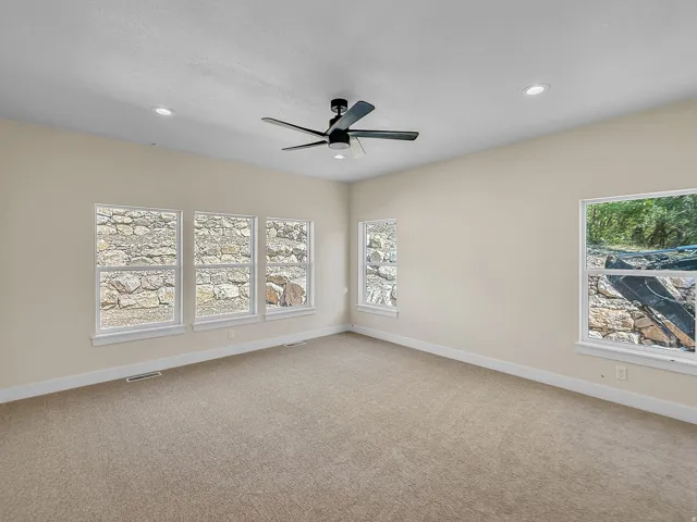 Empty room featuring light carpet, a ceiling fan, plenty of natural light, and recessed lighting