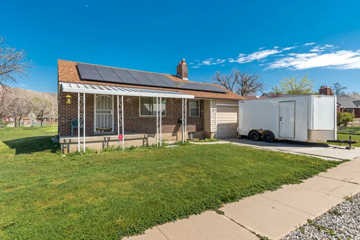 View of front of house with brick siding, roof mounted solar panels, a garage, and a front yard