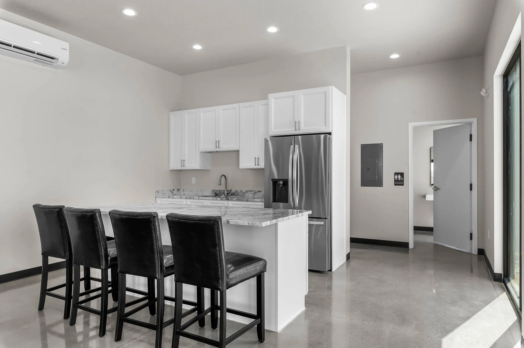 Kitchen with white cabinetry, stainless steel fridge with ice dispenser, concrete flooring, a kitchen breakfast bar, and recessed lighting