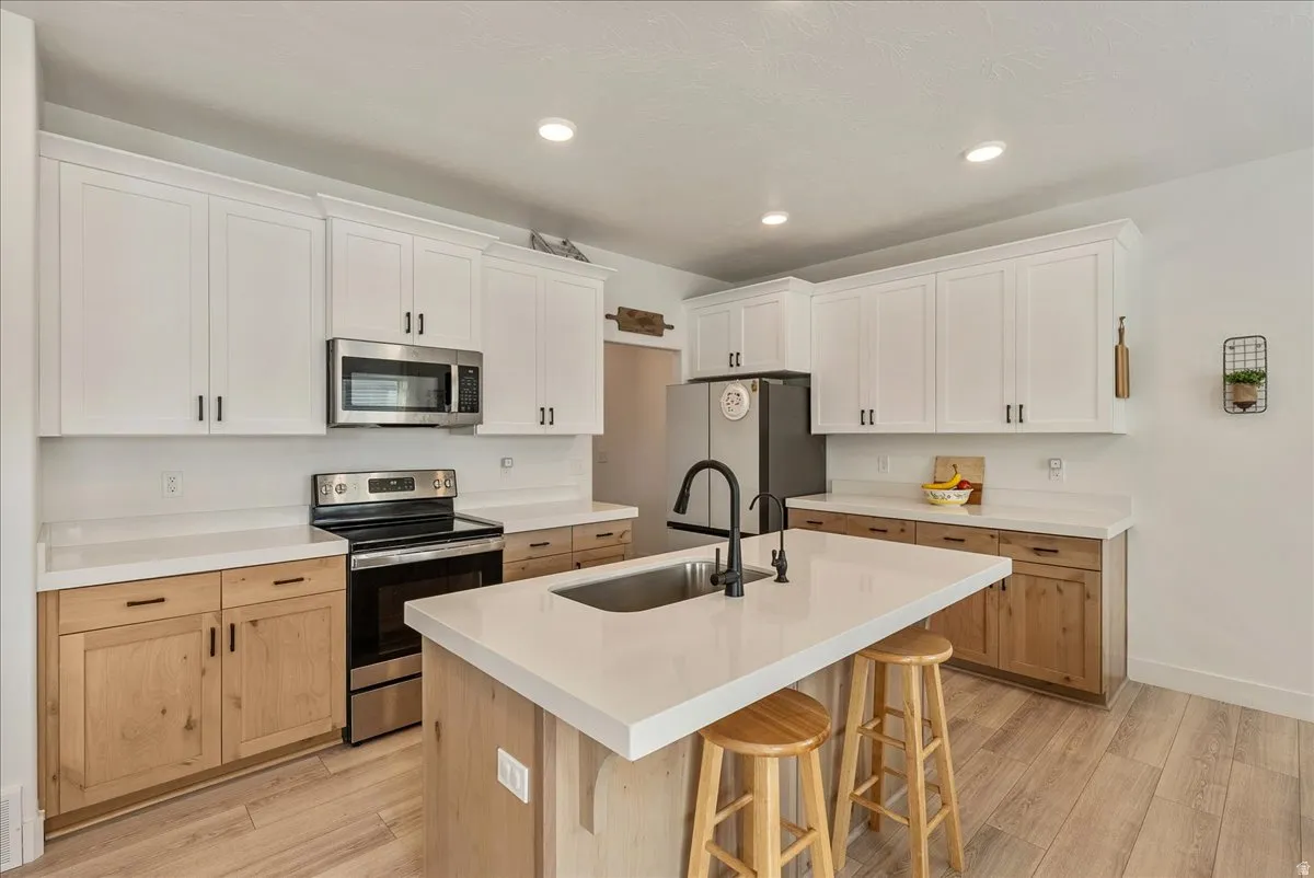 Kitchen featuring stainless steel appliances, light wood finished floors, a center island with sink, a kitchen bar, and two tone cabinetry