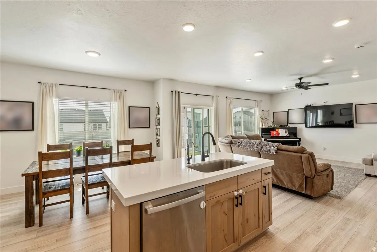 Kitchen with light wood-style floors, stainless steel dishwasher, a kitchen island with sink, open floor plan, and ceiling fan