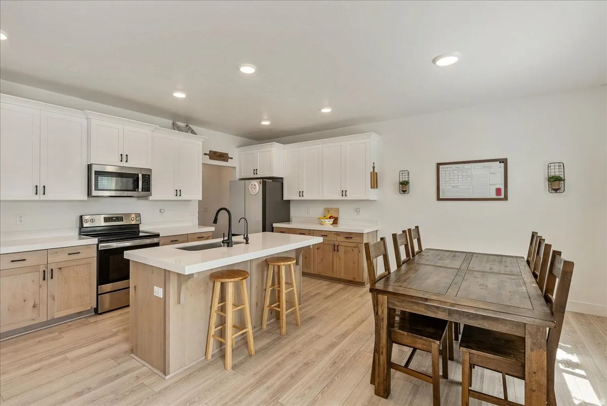 Kitchen with stainless steel appliances, a kitchen breakfast bar, an island with sink, dual tone cabinets, and light wood-style flooring