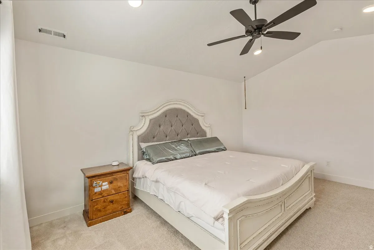 Bedroom with light colored carpet, a ceiling fan, vaulted ceiling, and recessed lighting