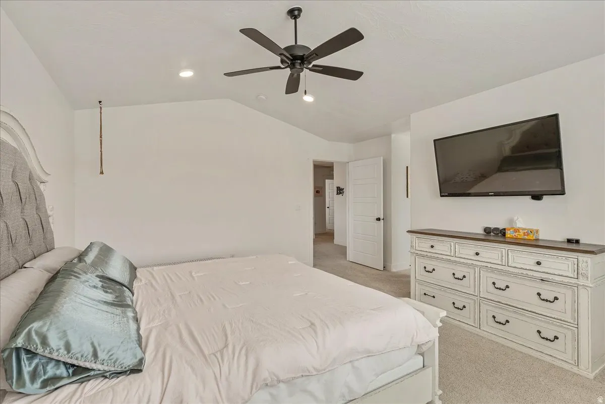 Bedroom with light colored carpet, lofted ceiling, and a ceiling fan