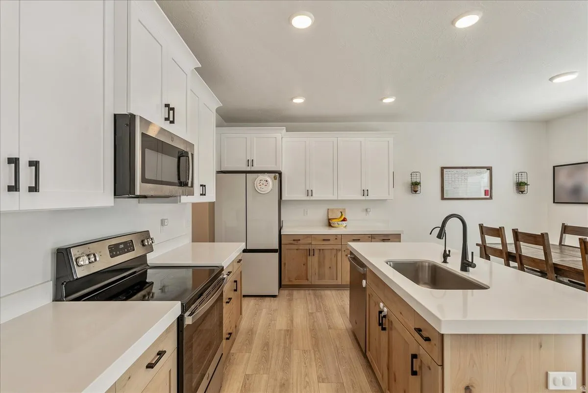Dual tone kitchen with stainless steel appliances, two tone cabinets, light wood-style floors, an island with sink, and recessed lighting