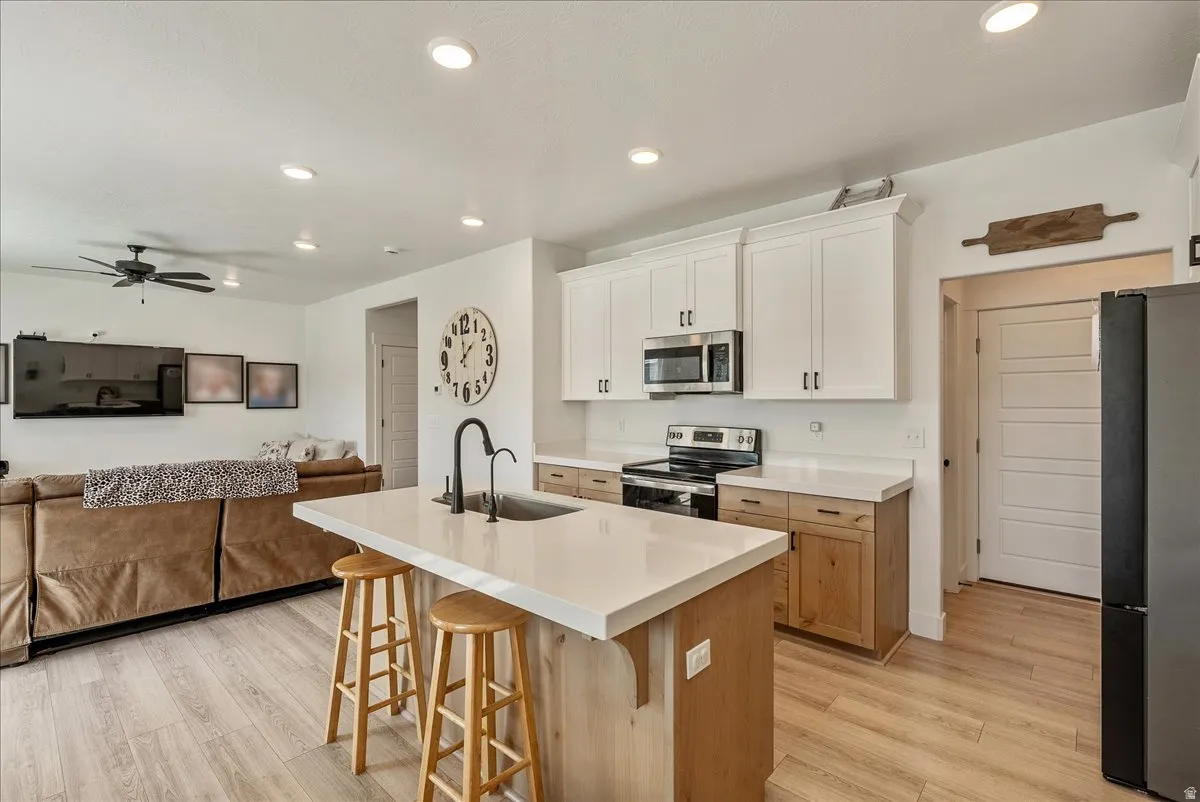 Kitchen featuring open floor plan, stainless steel appliances, a kitchen breakfast bar, light wood finished floors, and a center island with sink
