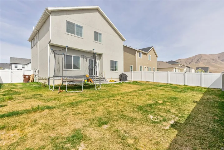 Rear view of house featuring a fenced backyard, stucco siding, a gate, a trampoline, and a mountain view