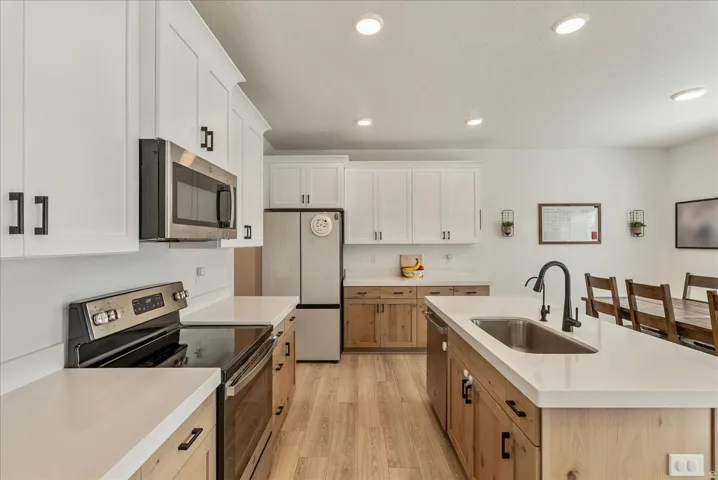 Dual tone kitchen with stainless steel appliances, two tone cabinets, light wood-style floors, an island with sink, and recessed lighting