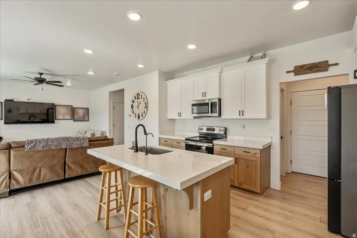 Kitchen featuring open floor plan, stainless steel appliances, a kitchen breakfast bar, light wood finished floors, and a center island with sink