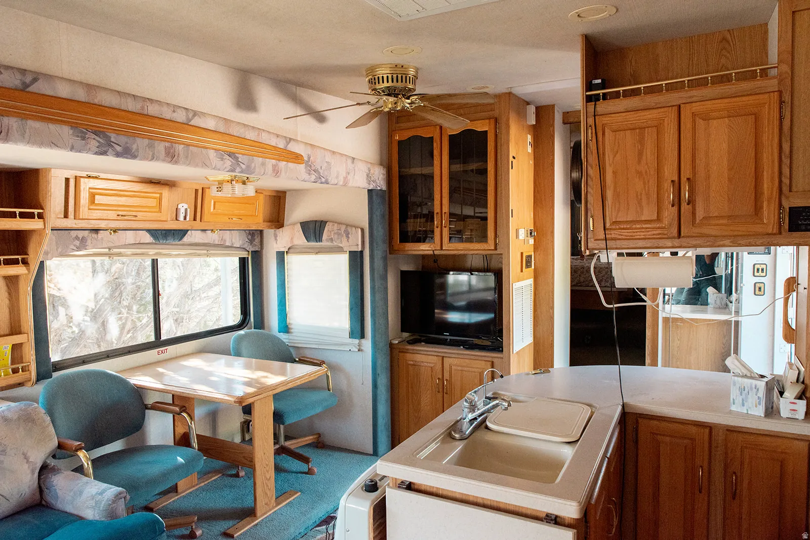 Kitchen featuring wood finish cabinetry, light countertops, glass fronted cabinets, and ceiling fan